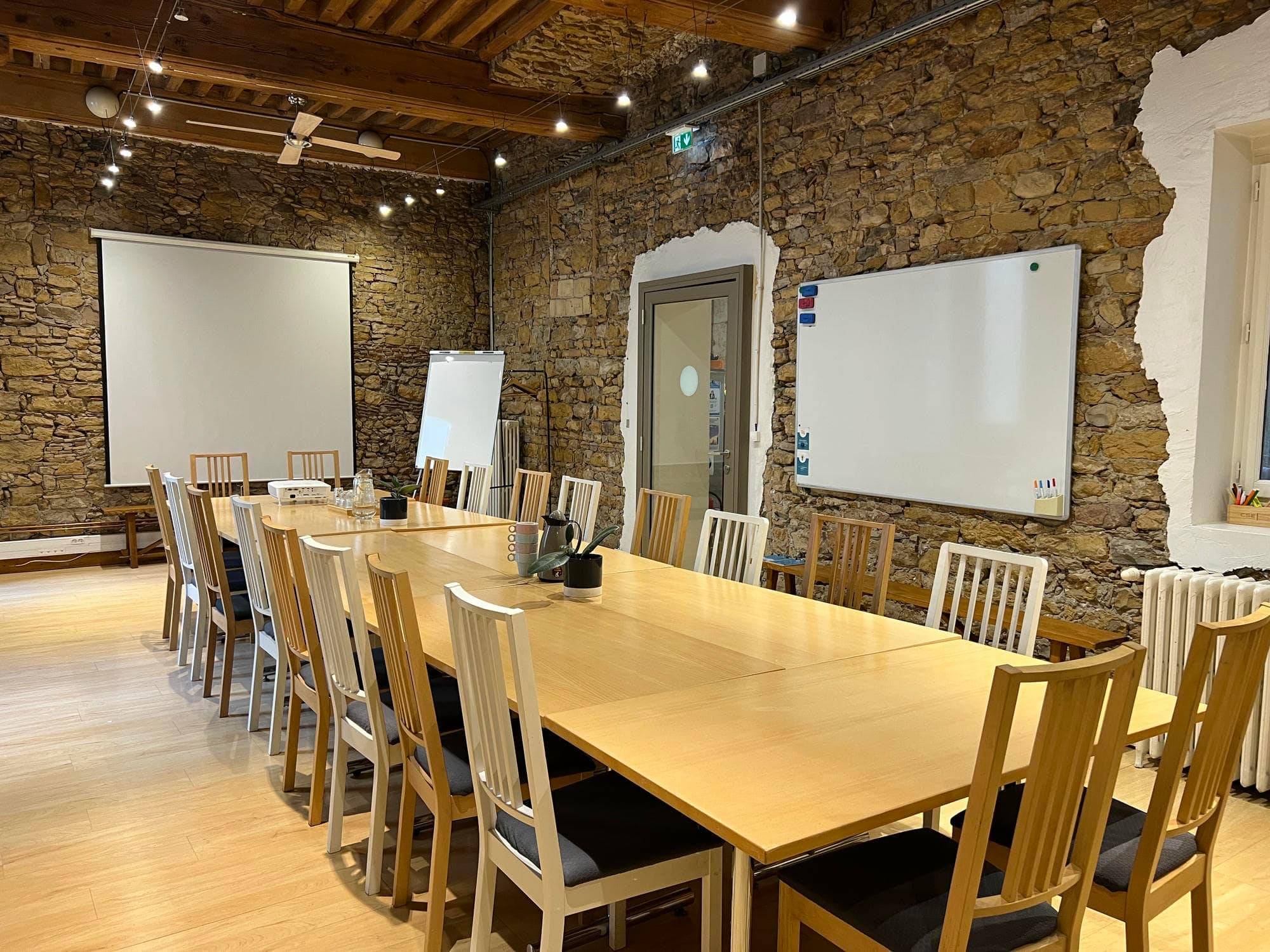 Grande salle aux murs en pierre avec tables modulables et écran, espace privatisable Lyon 1er Grande salle aux murs en pierre avec tables modulables et écran, espace privatisable Lyon 1er
