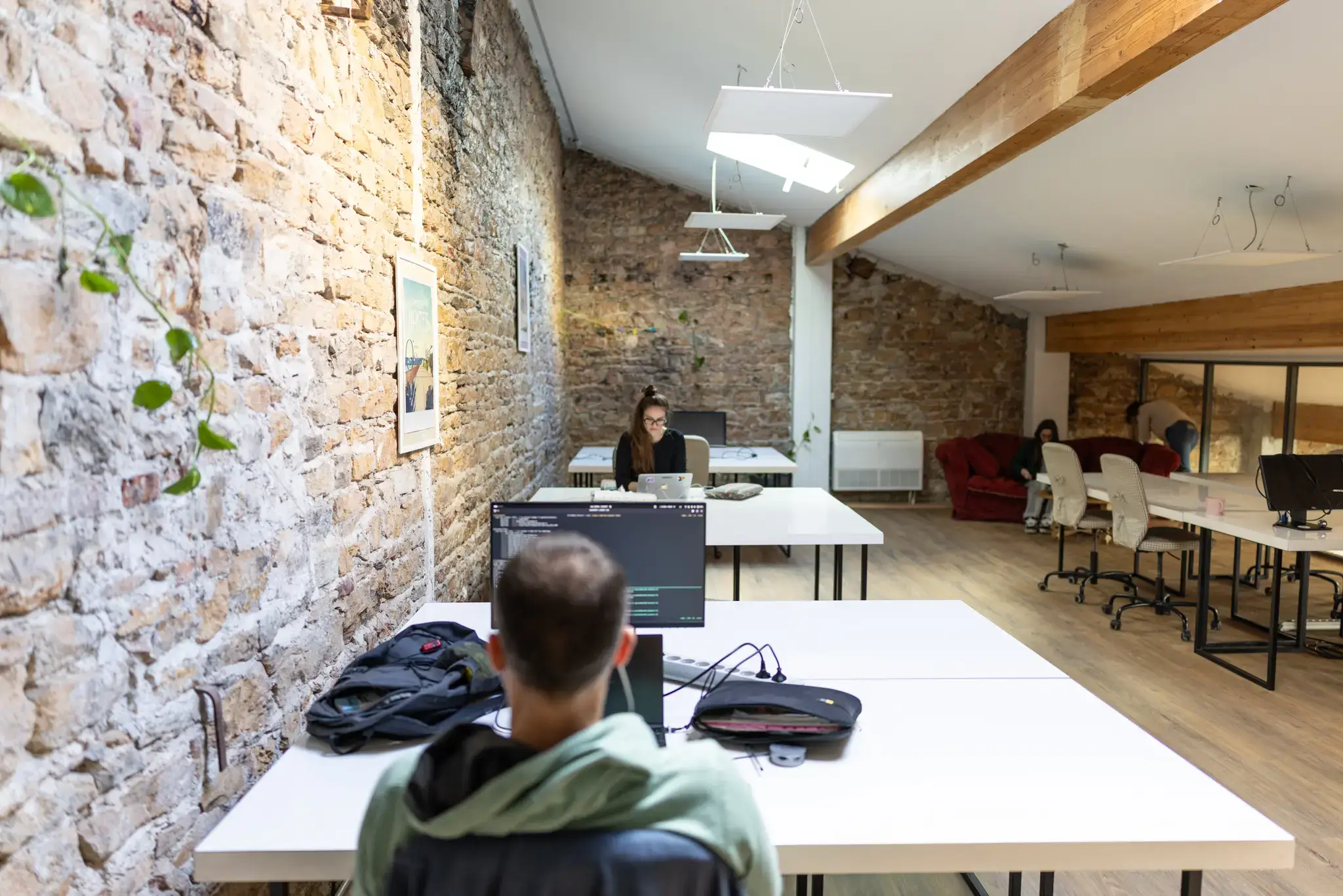 Coworker à son bureau attitré dans un espace aux murs en pierre, La Cordée Lyon Vaise